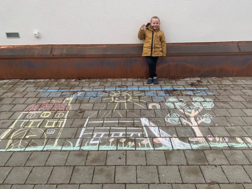 Kind steht vor einer bunten Straßenmalerei mit Häusern und Bäumen.