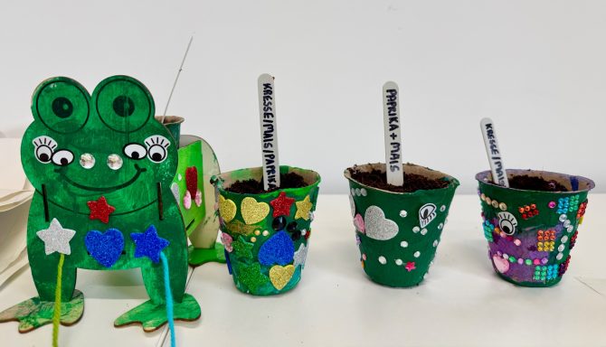 Bunte Töpfe mit Pflanzen und einem gebastelten grünen Frosch.