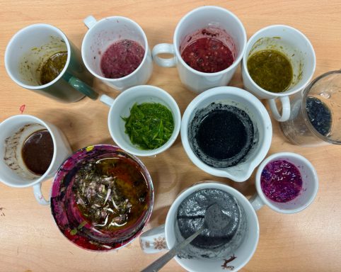 Verschiedene Tassen und Behälter mit bunten Farben und Farbmischungen auf einem Tisch.