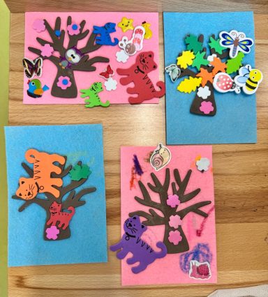 Bunte Bastelarbeiten mit Bäumen, Tieren und verschiedenen Dekorationen auf Papier.