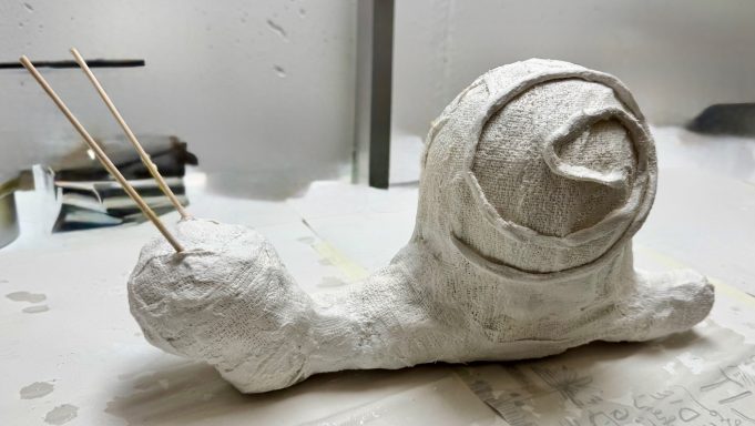 Eine skulpturale Schnecke aus Pappmaché mit zwei Fühlern aus Holz.