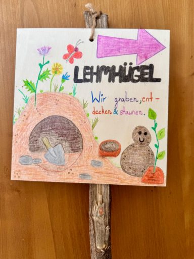 Bunte Zeichnung eines Lehnhügels mit Pflanzen, Tieren und einem Hinweis.